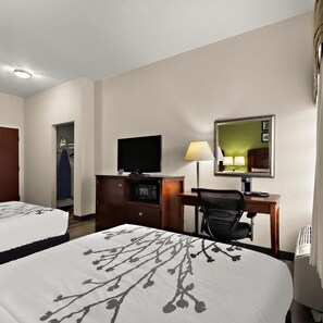 Ein Hotelzimmer mit zwei Betten, einem Schreibtisch, einem Fernseher, einem Spiegel und einer Lampe.