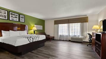 A hotel room with a large bed, a desk, a chair, a TV, and a window with curtains.