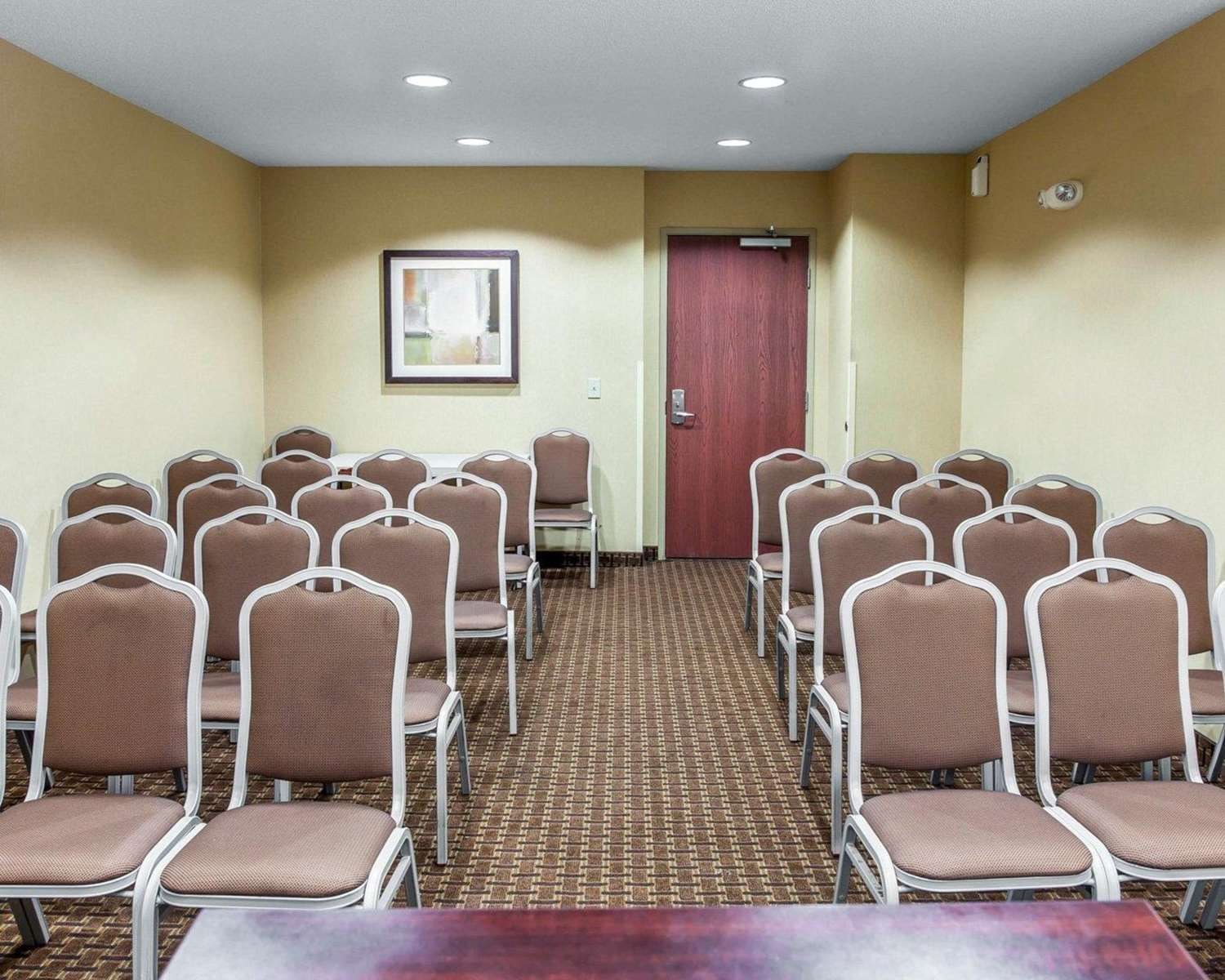 A conference room with rows of chairs, a door, and a framed picture on the wall.