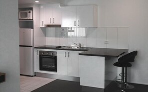 Cocina moderna con armarios blancos, horno empotrado, microondas y un taburete de bar.