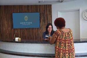 Een receptiebalie met een televisie waarop de naam van het hotel staat, een klok en een wandpaneel van hout.