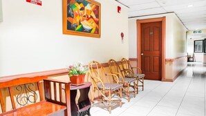 A hotel lobby with a reception desk, a 'No Smoking' sign, a colorful abstract painting, wicker chairs, and a wooden bench. - OYO 499 Le Pensione De San Jose (Tagbilaran)