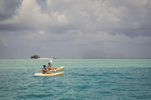 Two people in a kayak on turquoise water with a thatched-roof structure in the distance. - Decameron San Luis (San Andrés)
