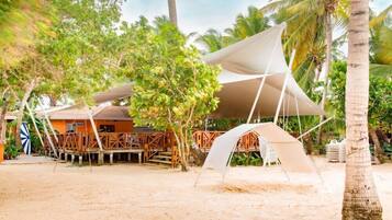Un resort frente a la playa con una zona cubierta, terraza de madera y palmeras.