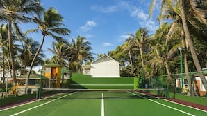A tennis court with a net, surrounded by palm trees and a small building. - Decameron San Luis (San Andrés)