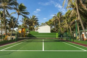 A tennis court with a net, surrounded by palm trees and a small building. - Decameron San Luis (San Andrés)