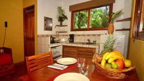 Une cuisine de taille réduite avec un coin repas, des meubles en bois et un panier de fruits sur la table.