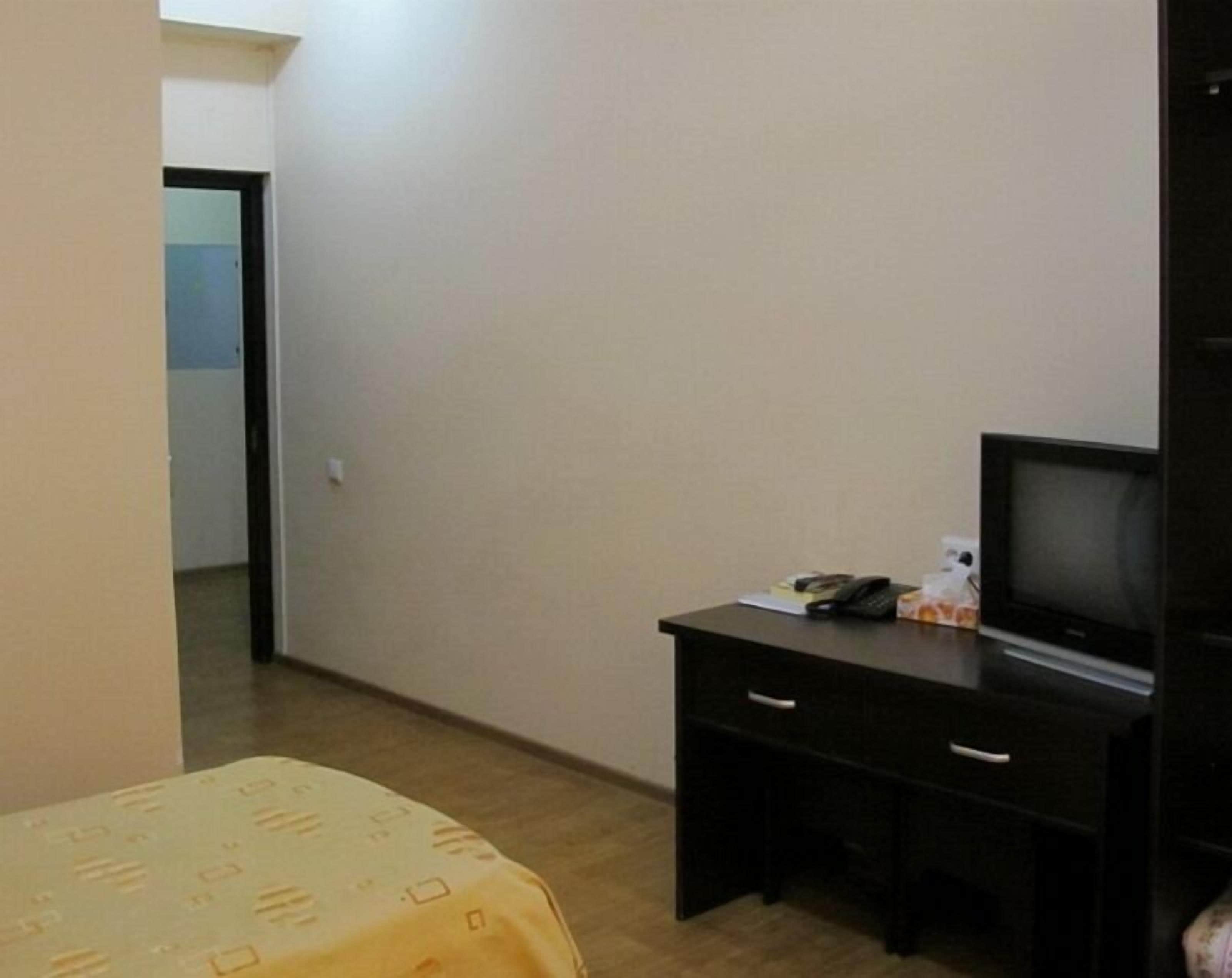 A small room with a bed, a desk with a television, and a door leading to another room.