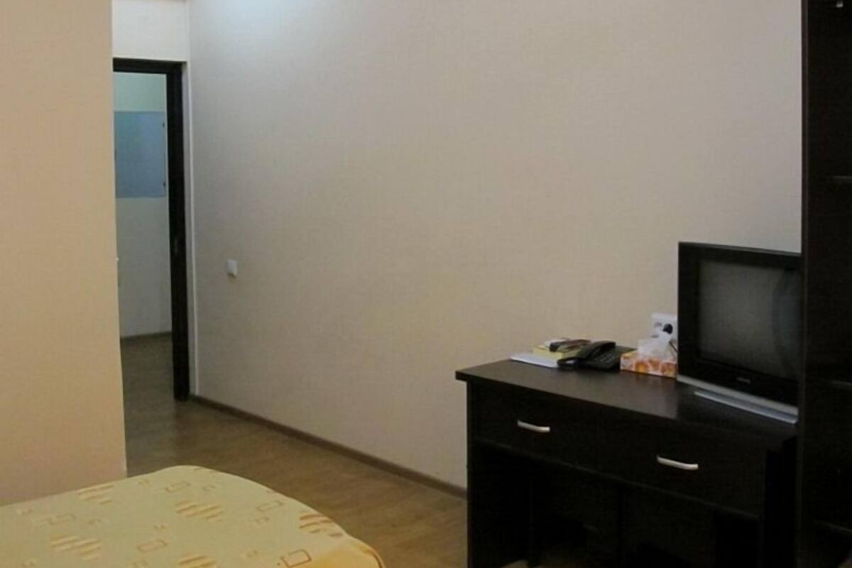 Une petite pièce comprenant un lit, un bureau avec une télévision et une porte donnant sur une autre pièce.
