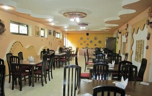 Un restaurant doté de nombreuses tables et chaises, d’un sol carrelé et d’un plafond décoratif.