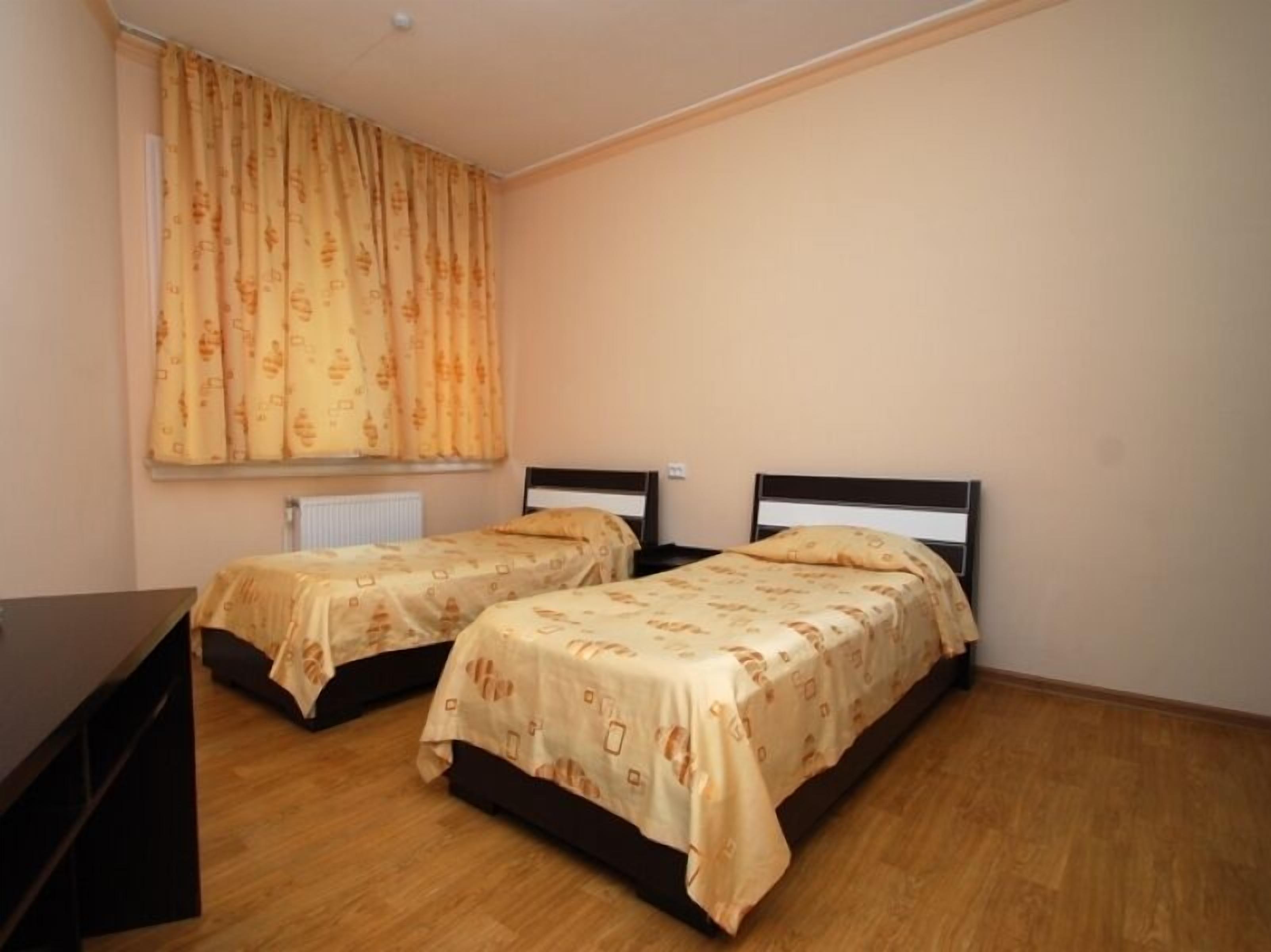 A room with two beds, a radiator, and a window with curtains.