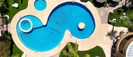 Una amplia piscina infinita con un diseño singular, rodeada de sillones de descanso y sombrillas.