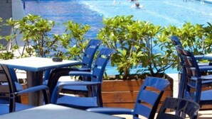 Una zona de piscina amb cadires i taules blaves, envoltada de plantes verdes petites.