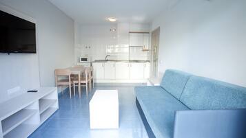 Una sala de estar moderna con un sofá azul, un mueble de entretenimiento blanco y una cocina al fondo.