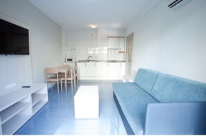 Een moderne woonkamer met een blauwe bank, een witte tv-kast, en een eethoek met een tafel en stoelen.
