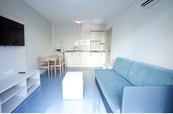 Een moderne woonkamer met een blauwe bank, een witte tv-kast, en een eethoek met een tafel en stoelen.