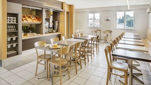 A dining area with multiple tables and chairs, a coffee station, and a view of the outside through large windows. - B&B Hotel Orange (Orange)