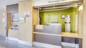 A B&B hotel reception area with a wooden reception desk, a green wall, and a sign that reads "Bienvenue chez B&B Hotels". - B&B Hotel Orange (Orange)