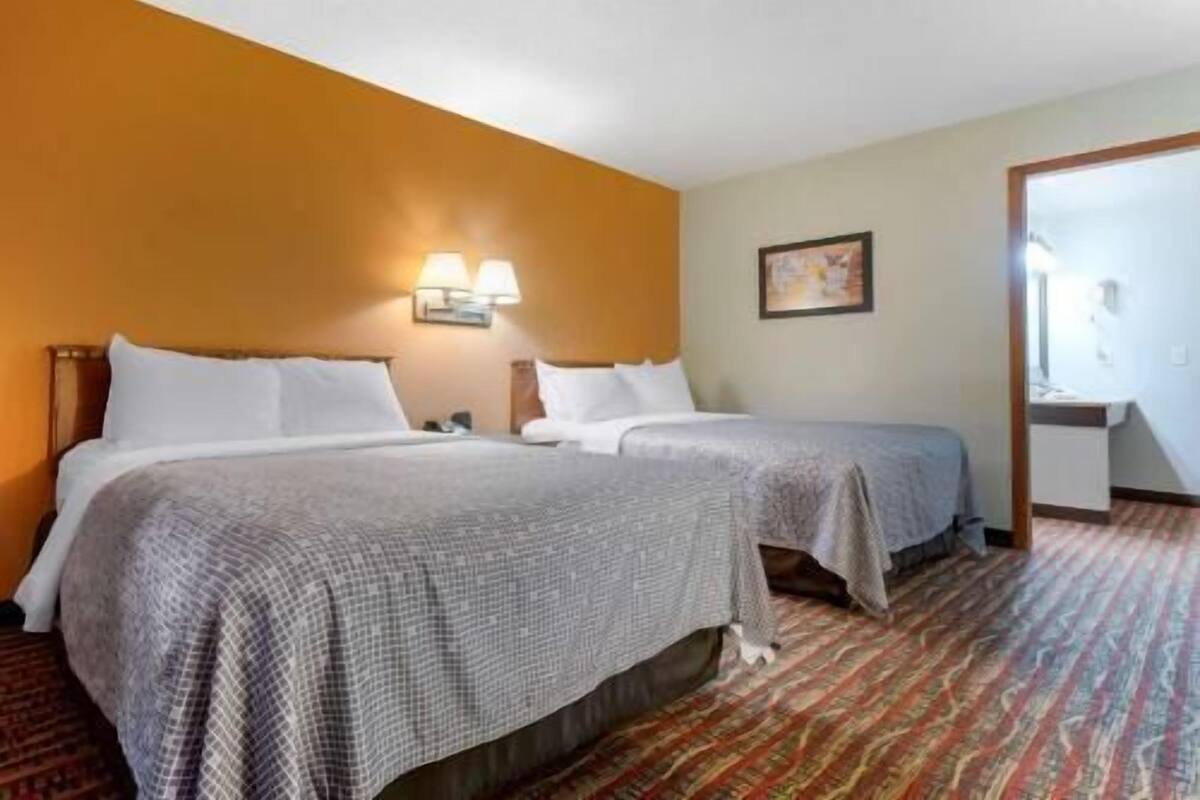 Habitación de hotel con dos camas, alfombra estampada, lámpara de pared y un cuadro enmarcado.