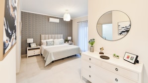 Une chambre à coucher moderne avec un grand lit, des tables de chevet, une commode, un miroir et un papier peint à motifs.