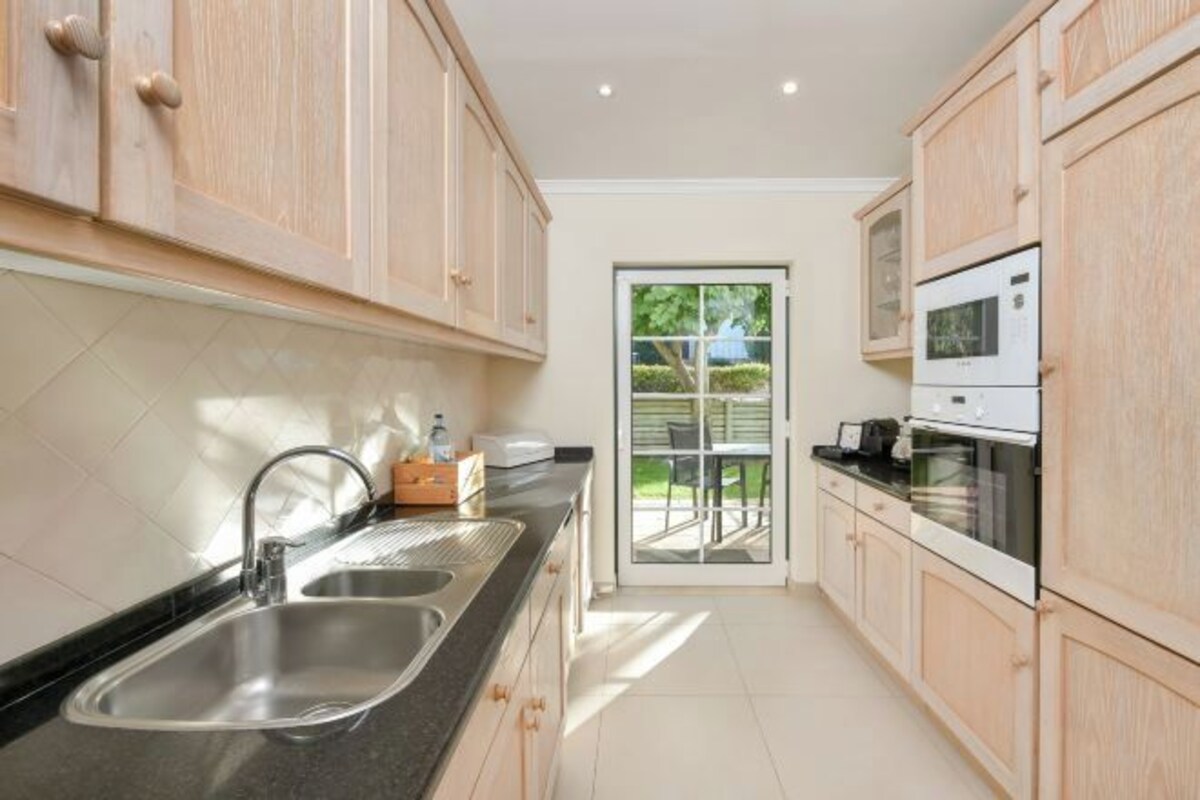 A modern kitchen with wooden cabinets, stainless steel sink, and built-in appliances.
