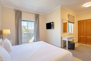Habitación de hotel con cama, escritorio, espejo, ventana con cortinas y puerta de madera.