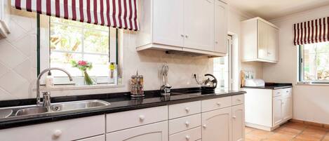 A kitchen with white cabinets, a black countertop, and striped window valances.