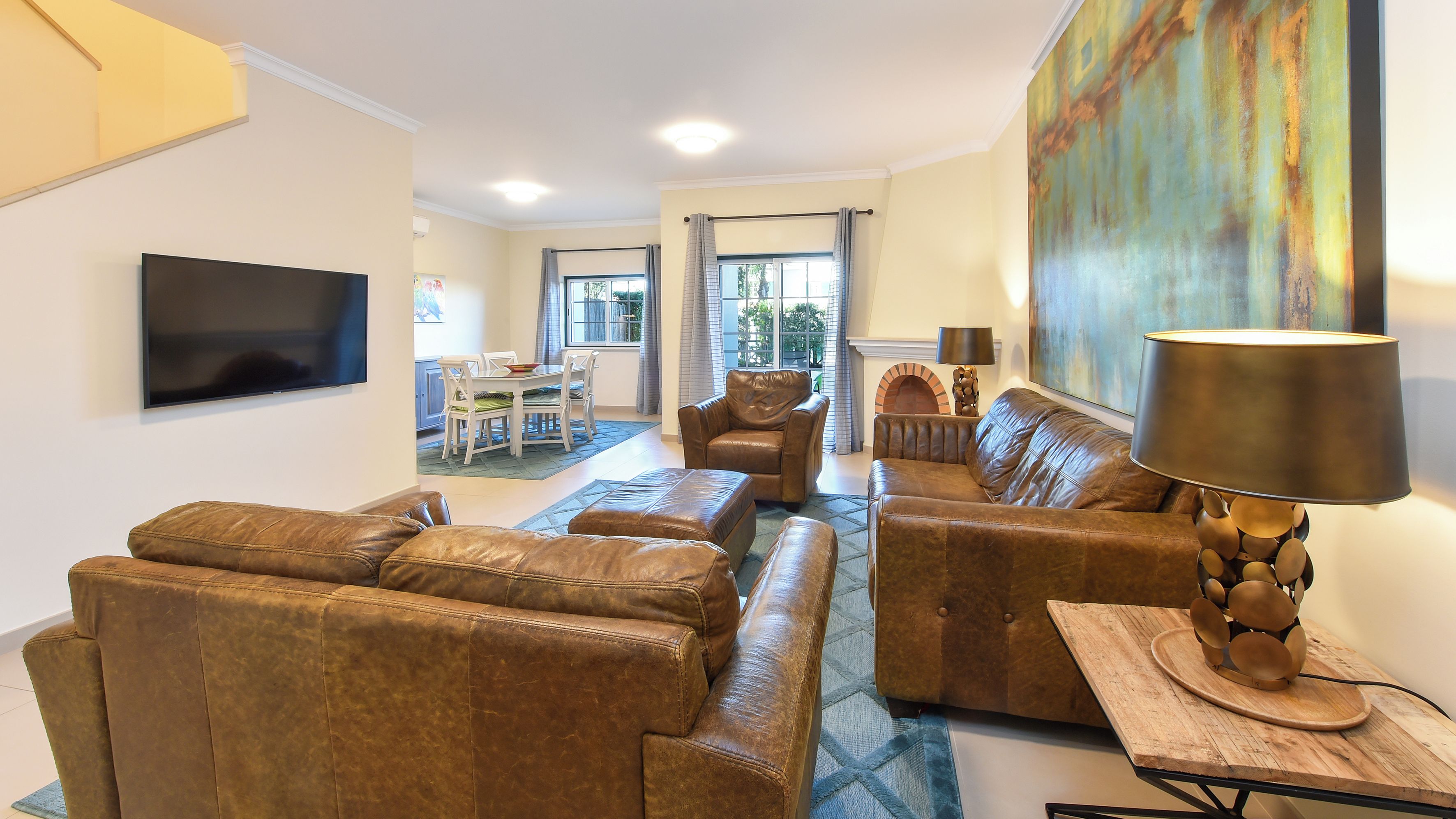 Een woonkamer met leren banken, een televisie en een eethoek met een tafel en stoelen.