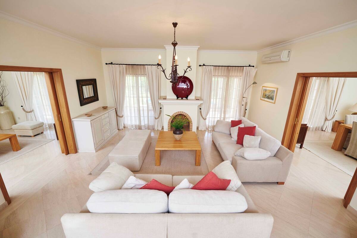 A spacious living room with a sofa set, a coffee table, a fireplace, and a chandelier.