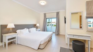 A hotel room with a large bed, two bedside tables with lamps, a desk with a chair, a mirror, and a view of the outside.