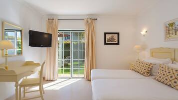 A hotel room with a bed, a desk, a chair, a television, a window with curtains, and a painting on the wall.