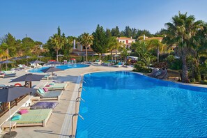 A large swimming pool with multiple lounge areas, a water slide, and surrounding palm trees. - Martinhal Quinta Do Lago Family Resort (Loulé)