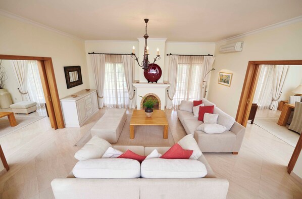 A spacious living room with a sofa set, a coffee table, a fireplace, and a chandelier. - Martinhal Quinta Do Lago Family Resort (Loulé)