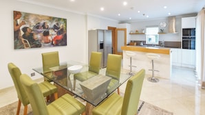 Une cuisine moderne avec un coin repas, comprenant une table en verre, des chaises vertes et un tableau au mur.