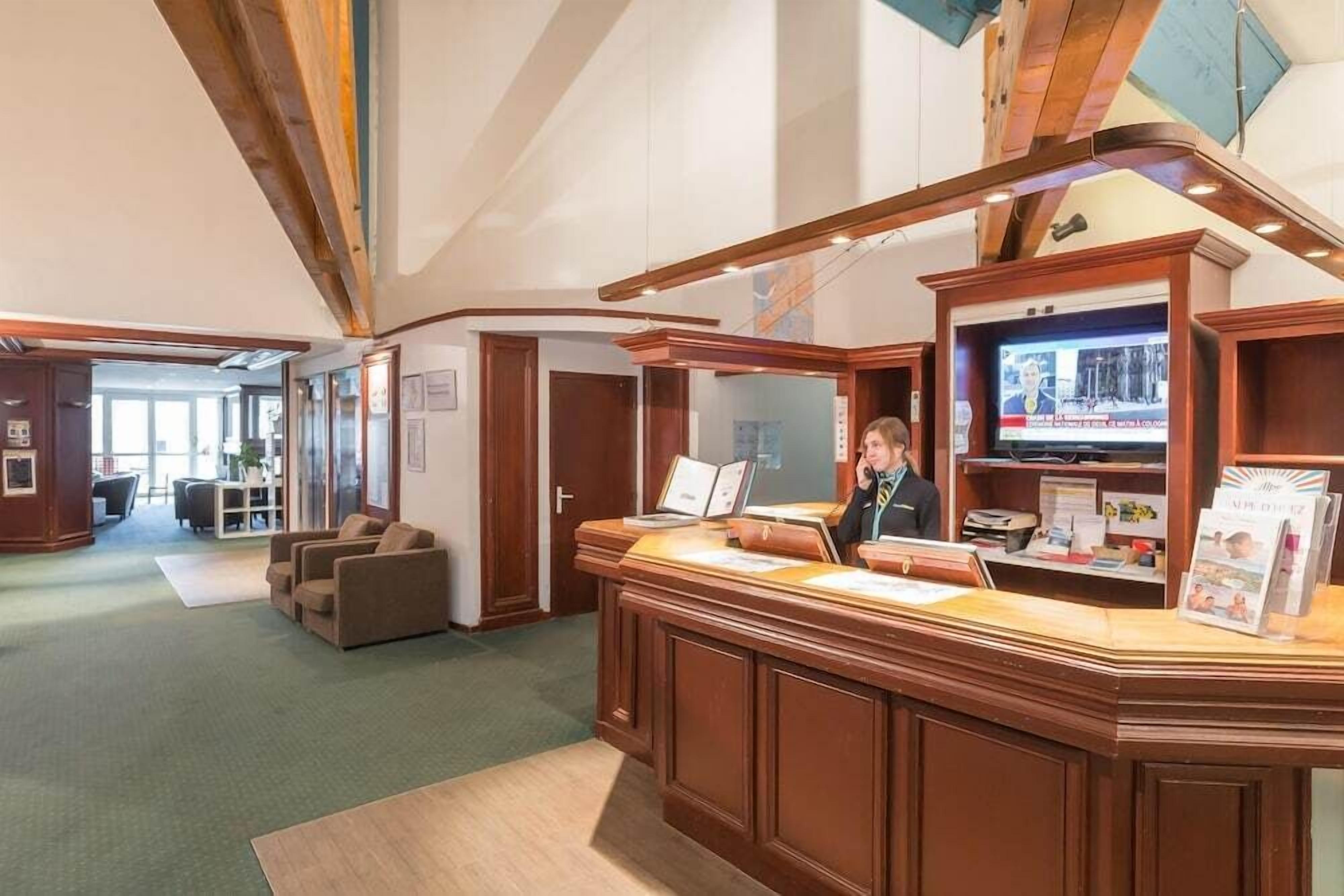 Un espace d’accueil comprenant un comptoir de réception en bois, un écran de télévision et un coin salon avec des canapés.
