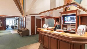 A reception area with a wooden reception desk, a television screen, and a seating area with sofas. - Residence Les Bergers (Huez)