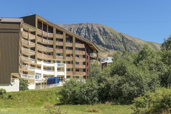 Un hotel de varios pisos con balcones, con montañas como telón de fondo.