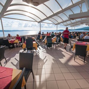 An outdoor dining area with tables and chairs, overlooking a body of water. - Lavanda Hotel (Sali)