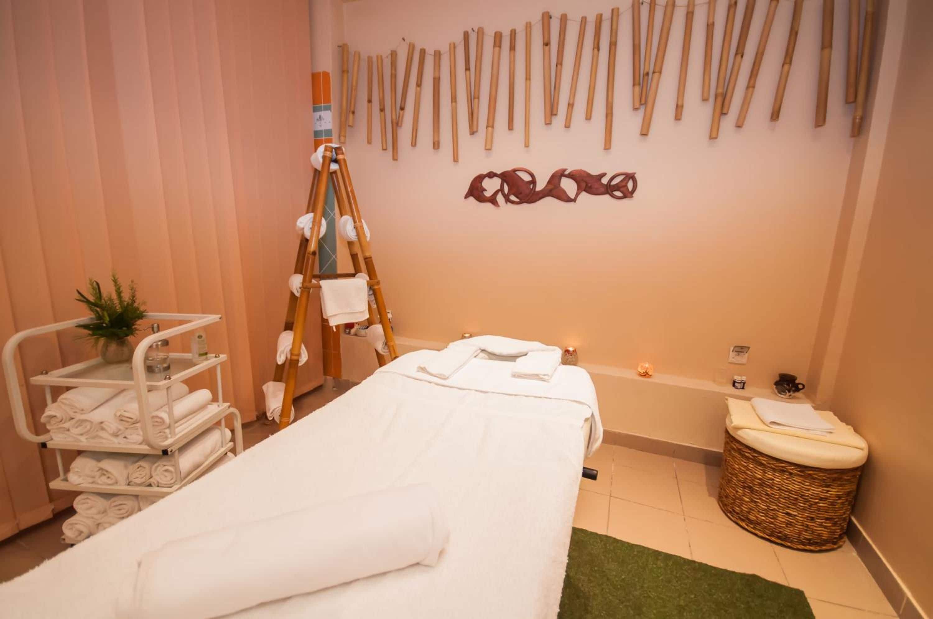 Een spa ruimte met een massagetafel, een plank met handdoeken, een kleine plant en een houten wandrek.