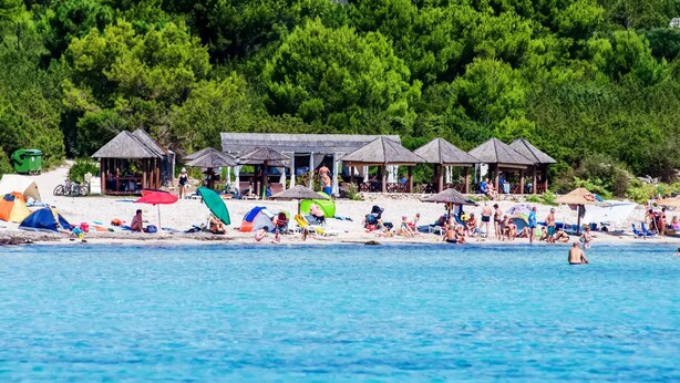 Una platja amb diverses cabanes de bany, un tram de sorra i mar blau cristal·lí.