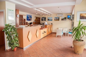 A reception area with a wooden counter, white chairs, and potted plants. - Lavanda Hotel (Sali)