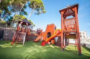 A wooden play structure with slides and climbing areas, surrounded by a fenced yard with artificial grass. - Lavanda Hotel (Sali)