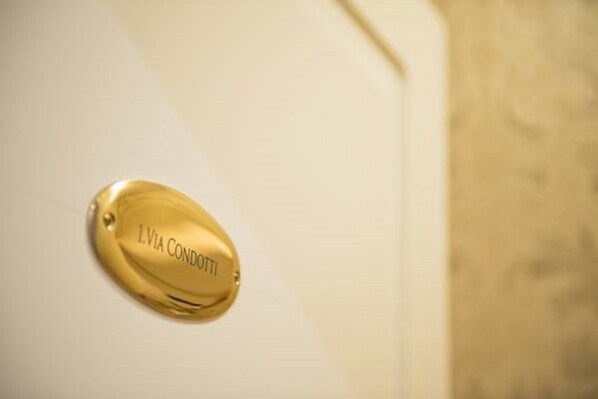 A gold-colored nameplate with the inscription "L'VIA CONDOTTI" on a white surface. - Relais Bocca di Leone (Rome)