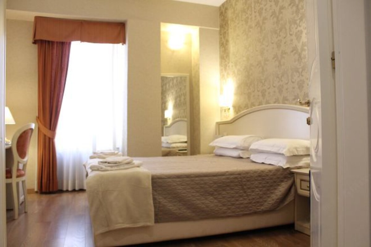 A hotel room with a bed, a chair, a desk, and a mirror.