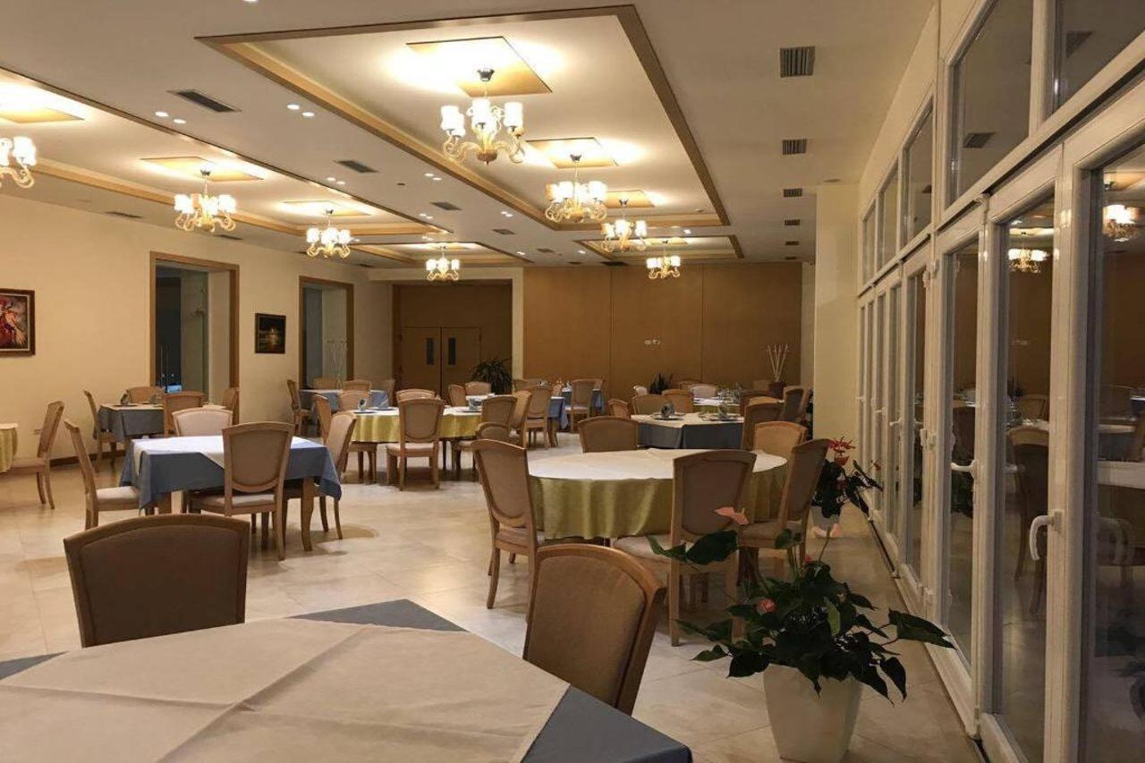 A dining area with multiple tables and chairs, chandeliers, and a view through glass doors.