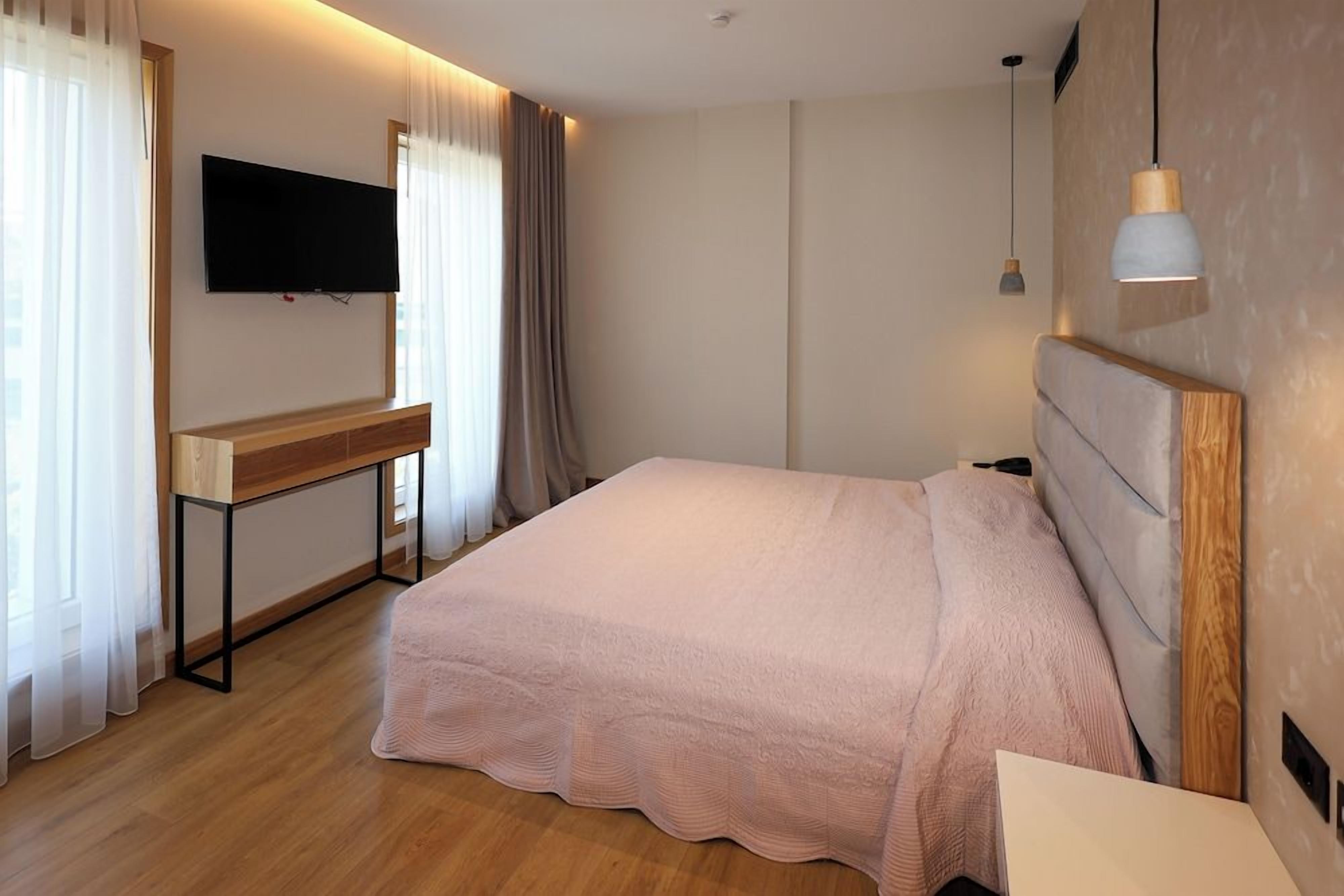 Un dormitorio con una cama, un televisor montado en la pared, un escritorio y una mesita de noche.