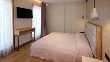 Un dormitorio con una cama, un televisor montado en la pared, un escritorio y una mesita de noche.