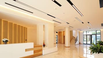 Un área de recepción moderna con piso de mármol, un mostrador de recepción y una escalera que conduce a los pisos superiores.