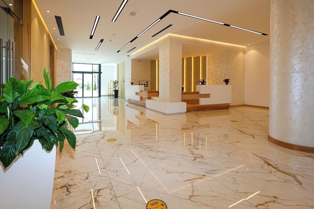 Un'hall d'albergo con pavimento in marmo, reception e un'ampia pianta in vaso.