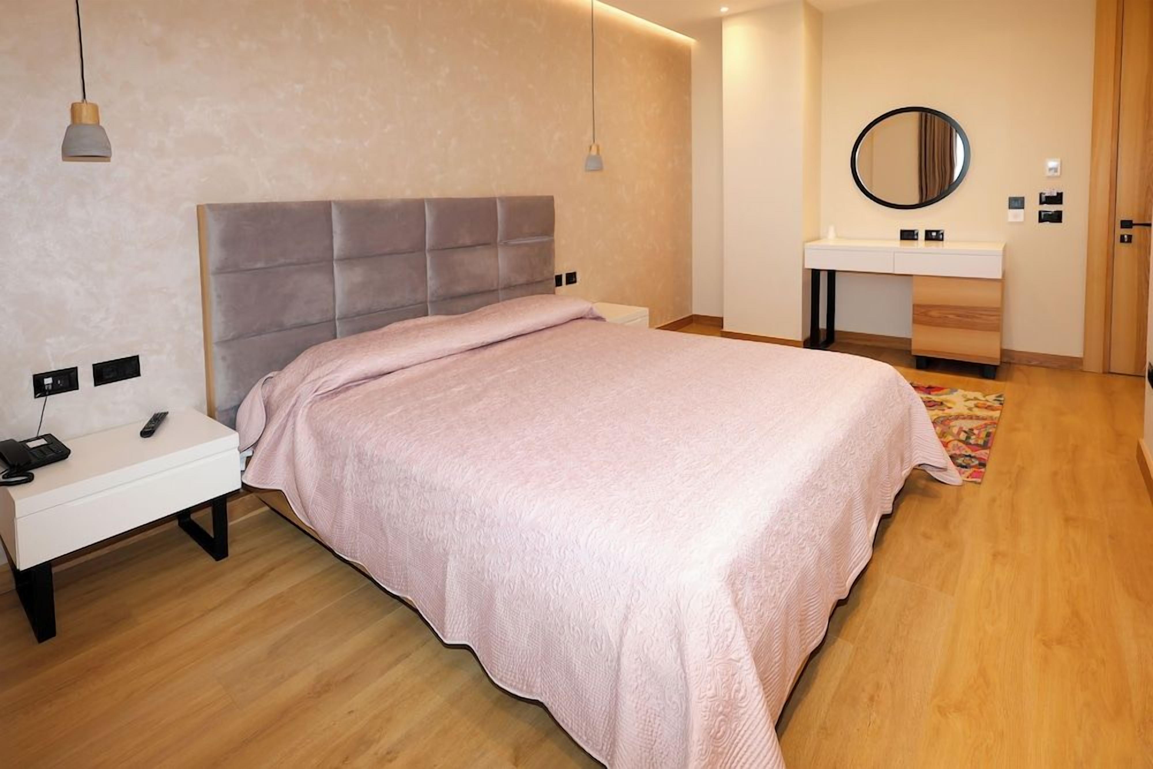 A modern bedroom with a bed, bedside table, and a vanity with a mirror.